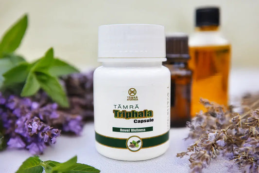 Tamra Ayurveda Triphala Capsule bottle with herbs and flowers on a light background