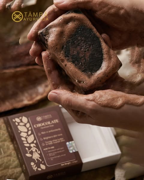 Chocolate soap held in hands with Tama Ayurveda branding in the background