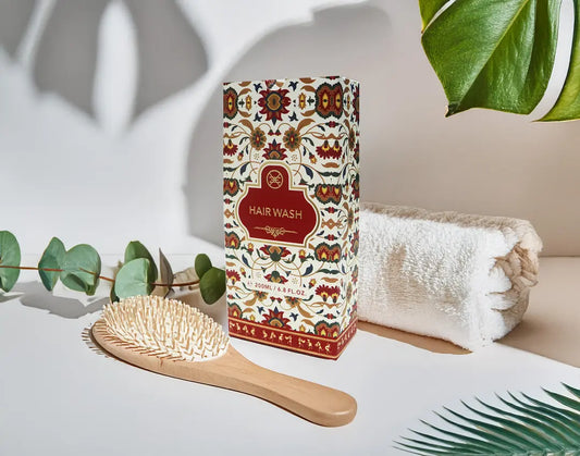Hair wash packaging with a brush and towel on a light surface with greenery.