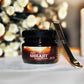 Jar of Tamra Ayurveda Shilajit with a spoon on a decorative surface with flowers and a candle.