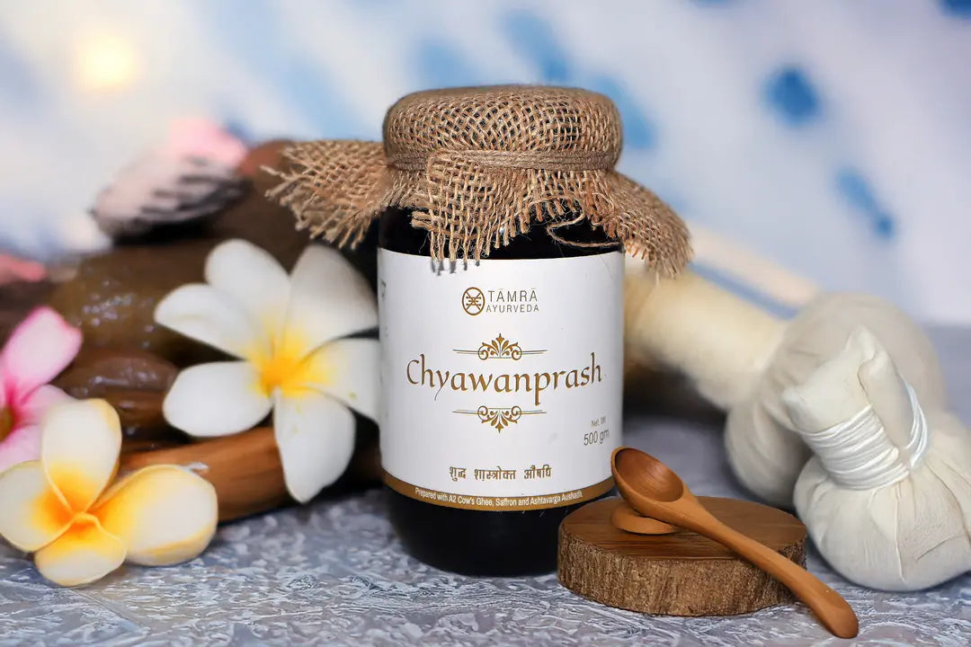 Jar of Tamra Chyawanprash with flowers and a spoon on a textured surface