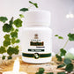 White bottle labeled 'TAMRA Brahmi' on a decorative surface with green leaves and candles.