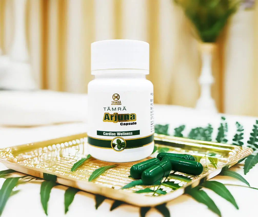 White bottle labeled 'TAMRA Arjuna' on a decorative tray with green capsules.