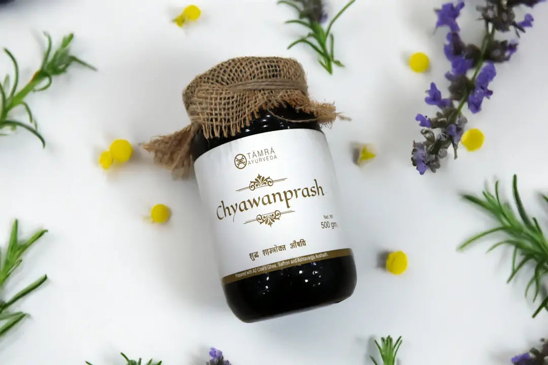 Jar of Tamra Chyawanprash with burlap lid on a white background with herbs.