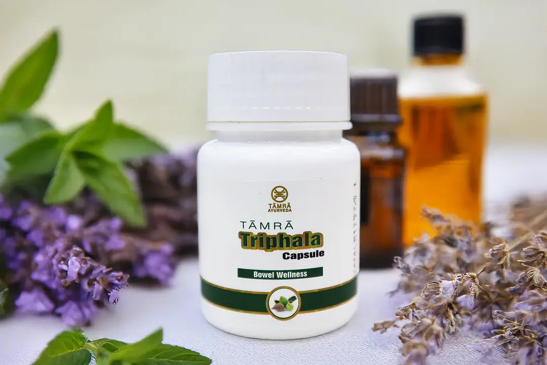 Tamra Ayurveda Triphala Capsule bottle with herbs and flowers on a light background