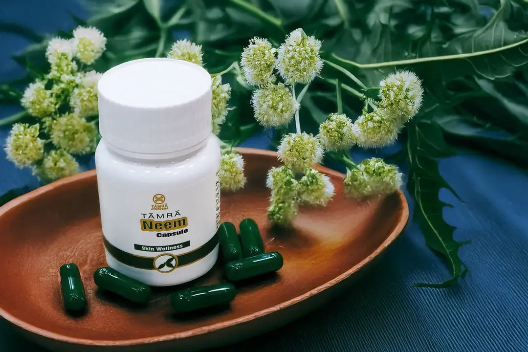 Tamra Neem supplement bottle with green capsules on a wooden plate surrounded by flowers and leaves.