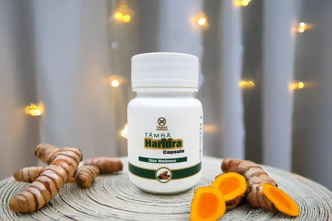 White bottle of Tamra Haridra Capsule with turmeric slices on a wooden surface.